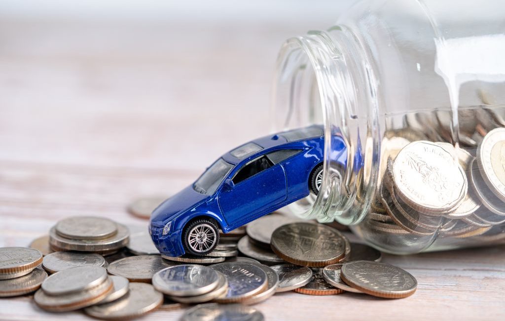 Toy car coming out of a tipped glass jar filled with coins, symbolizing car savings or auto financing.